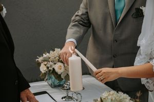 Hands lighting a unity candle during wedding ceremony with floral arrangements on table.