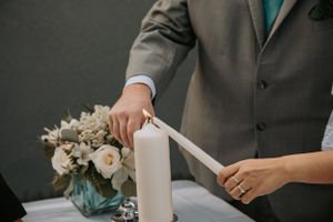 Close-up of hands lighting unity candle with white roses in turquoise vase.