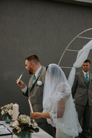 Wedding ceremony moment during unity candle lighting under white arch outdoors.