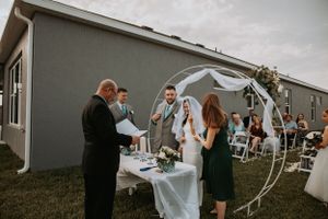 Outdoor wedding ceremony with white arch and floral decorations on cloudy day.