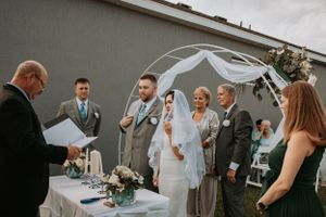Wedding party members in gray suits and white dresses gather outside a building during the ceremony.