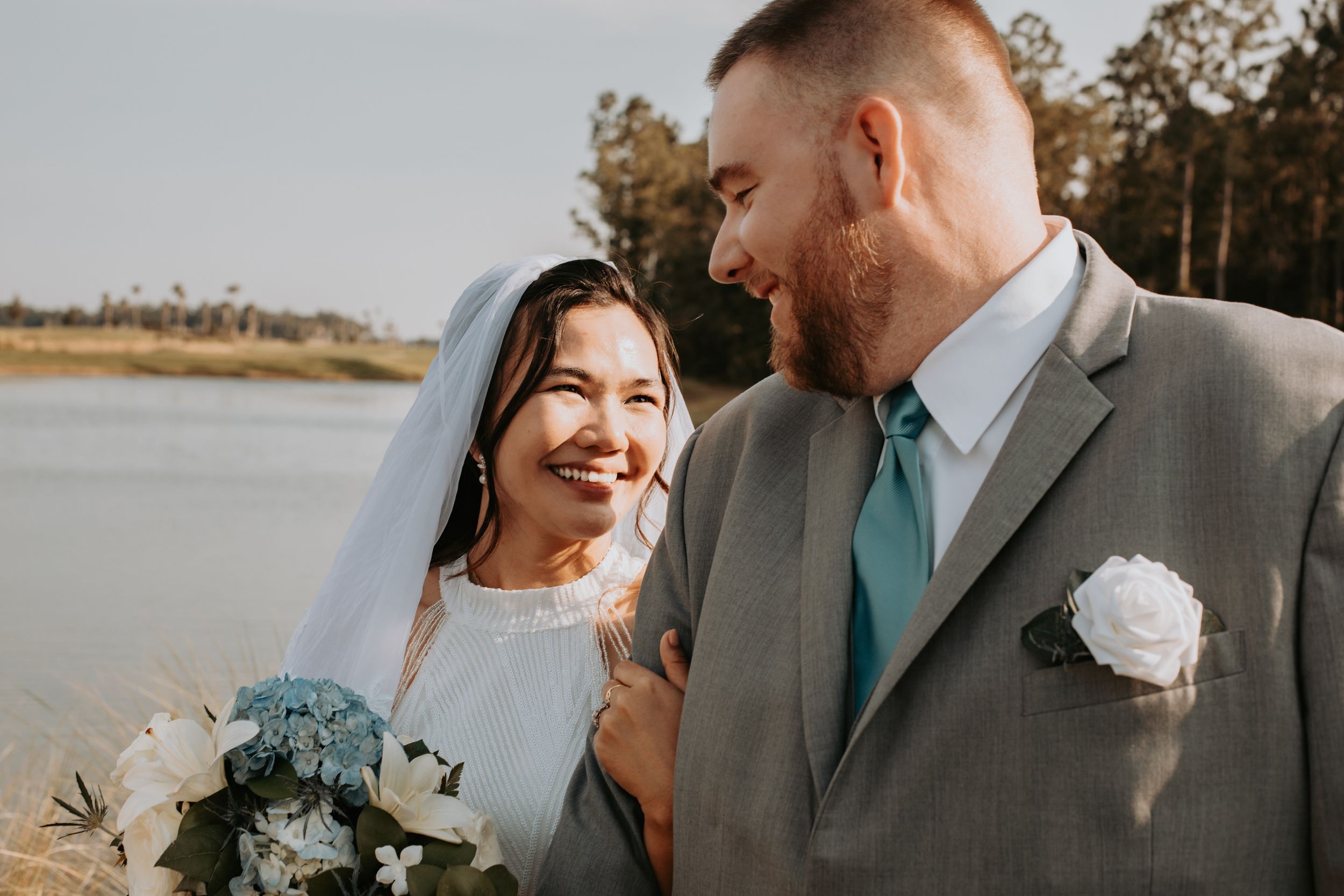 Couple sharing joyful moment outdoors with water and trees in background.