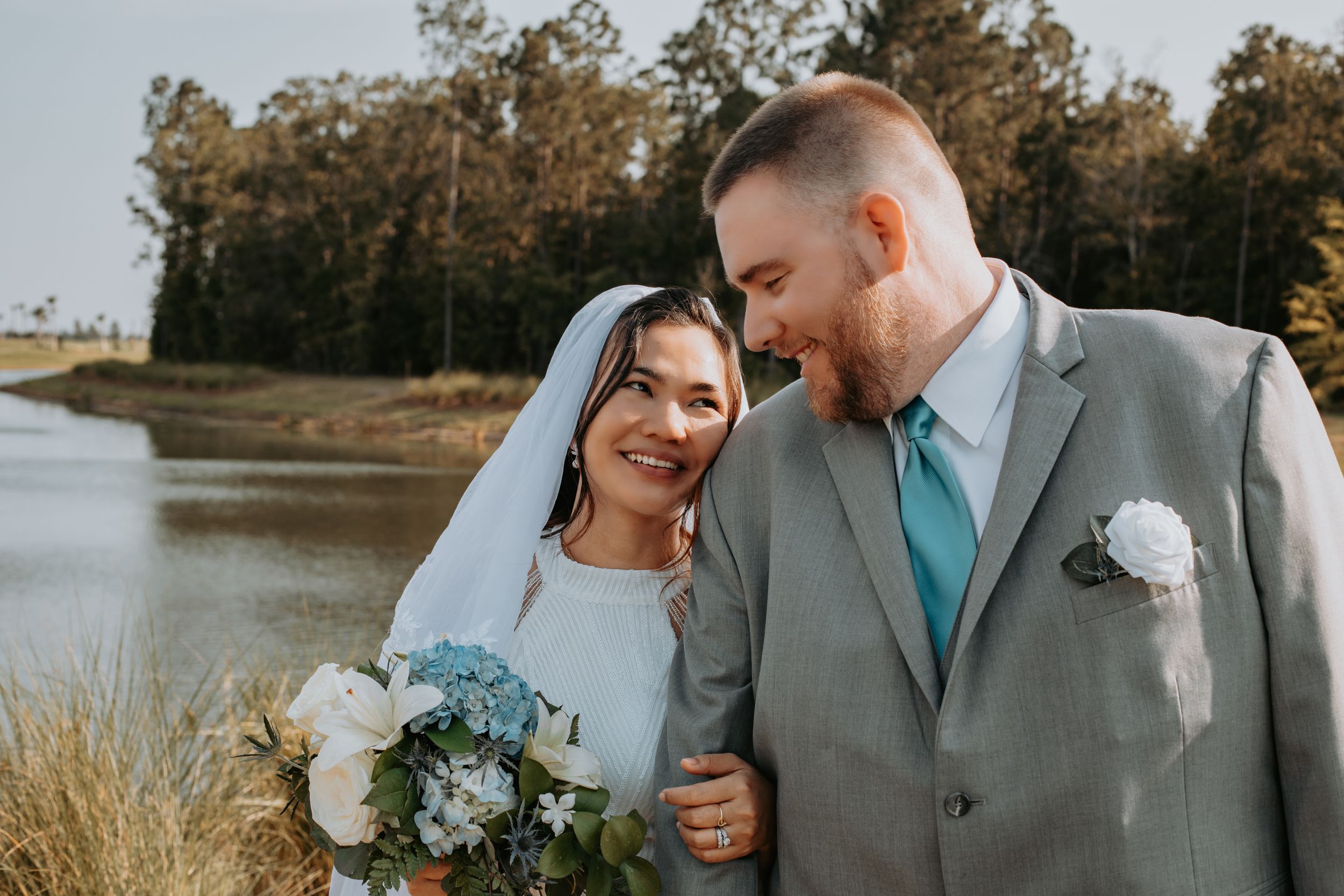 A couple in wedding attire share an intimate moment by a waterfront.