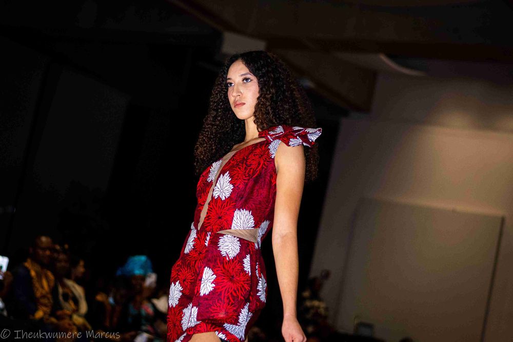 Model walks the runway in a red floral dress during a fashion show.