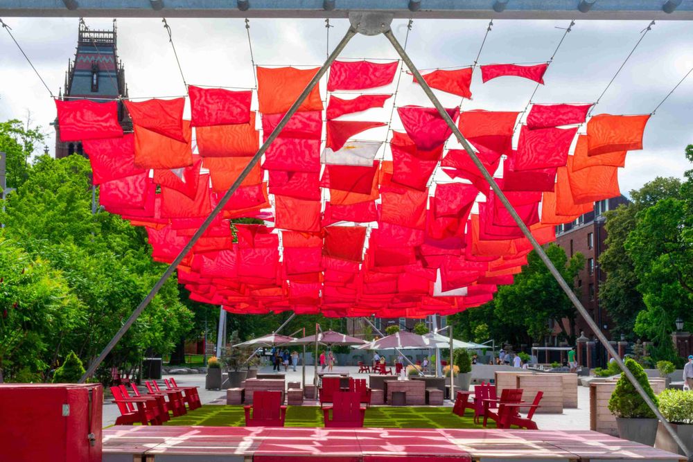 Red fabric canopies provide shade over outdoor seating area surrounded by green trees.