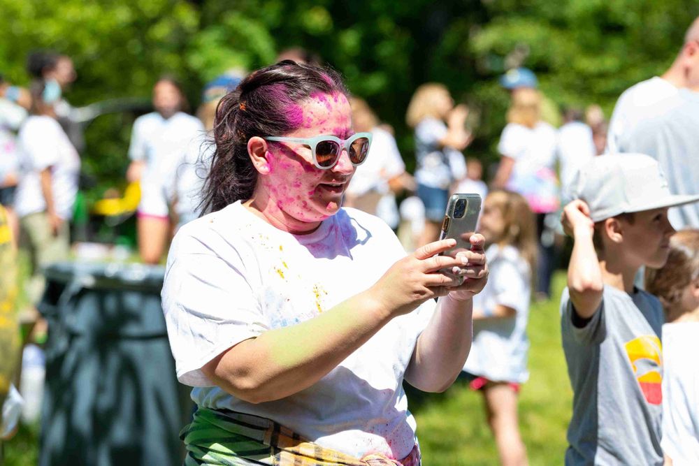 A participant at a color run event checks their phone while covered in pink powder during an outdoor festival.
