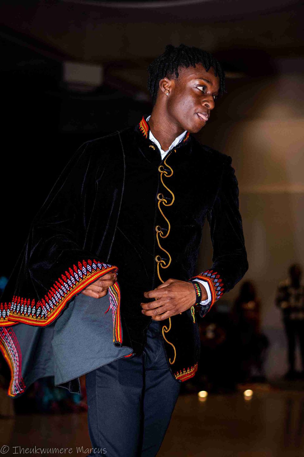 A fashion model wears a stylish black jacket with ornate trim during a runway show.