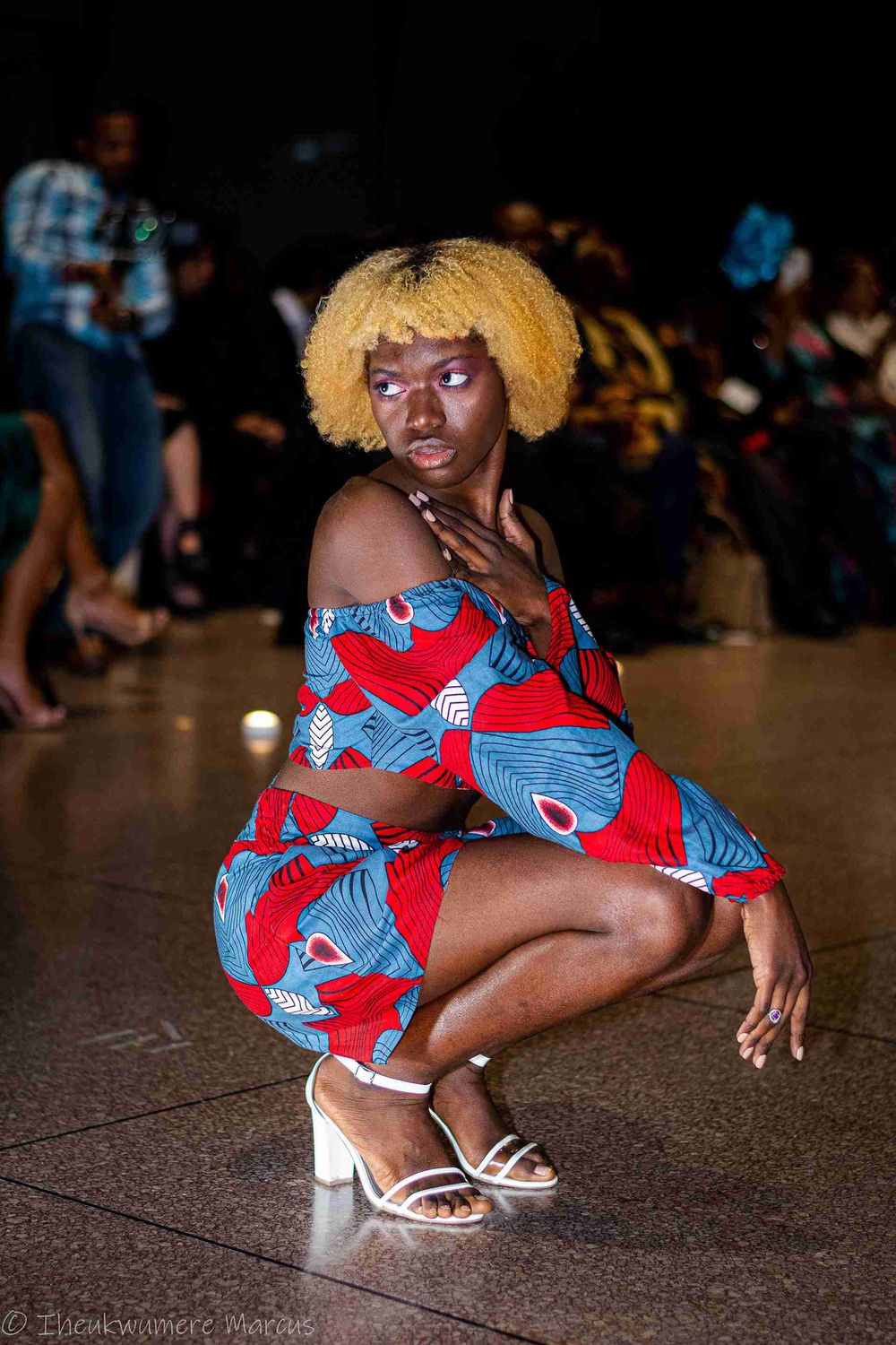 A dancer in a vibrant red and blue patterned dress and blonde hair strikes a dynamic pose on a dance floor.