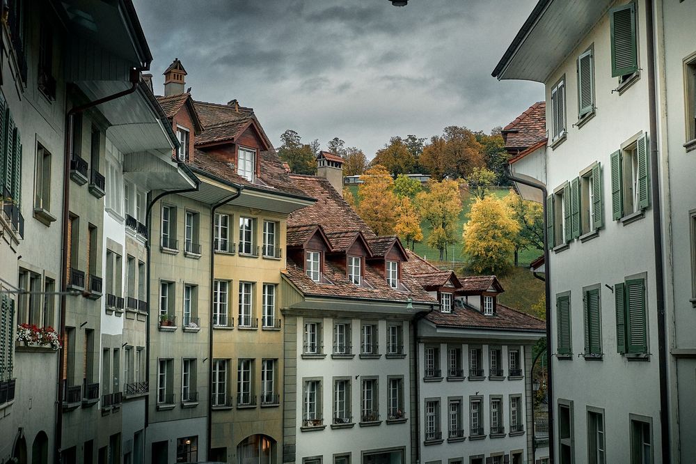 Historic cobblestone street lined with traditional white buildings and red roofs in a European town under moody skies.