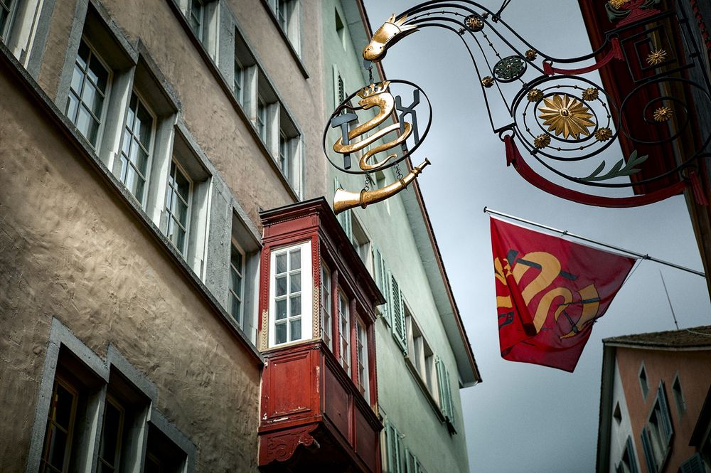 Row of vintage shop signs and hanging business markers on a historic European building facade.