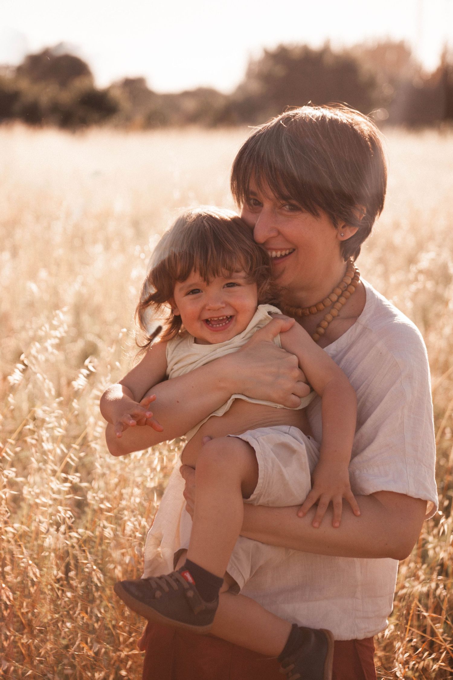 bimbo con mamma incinta, sorella, pancione, sessione fotografica esterna, campo fiori spighe, abbraccio mamma figlia, fotografia di famiglia