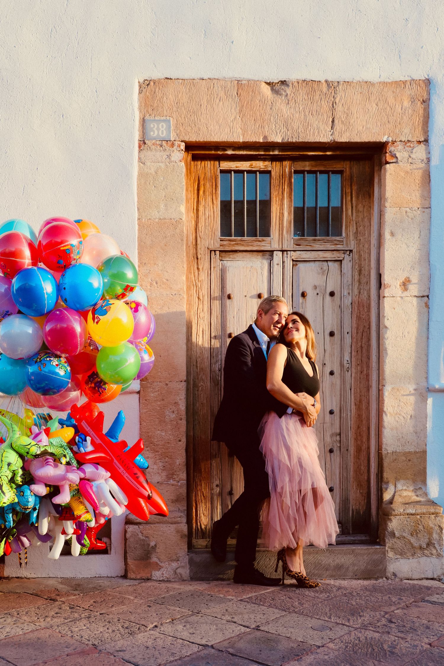 A couple posing by a rustic wooden door with colorful balloons creating a vibrant contrast.