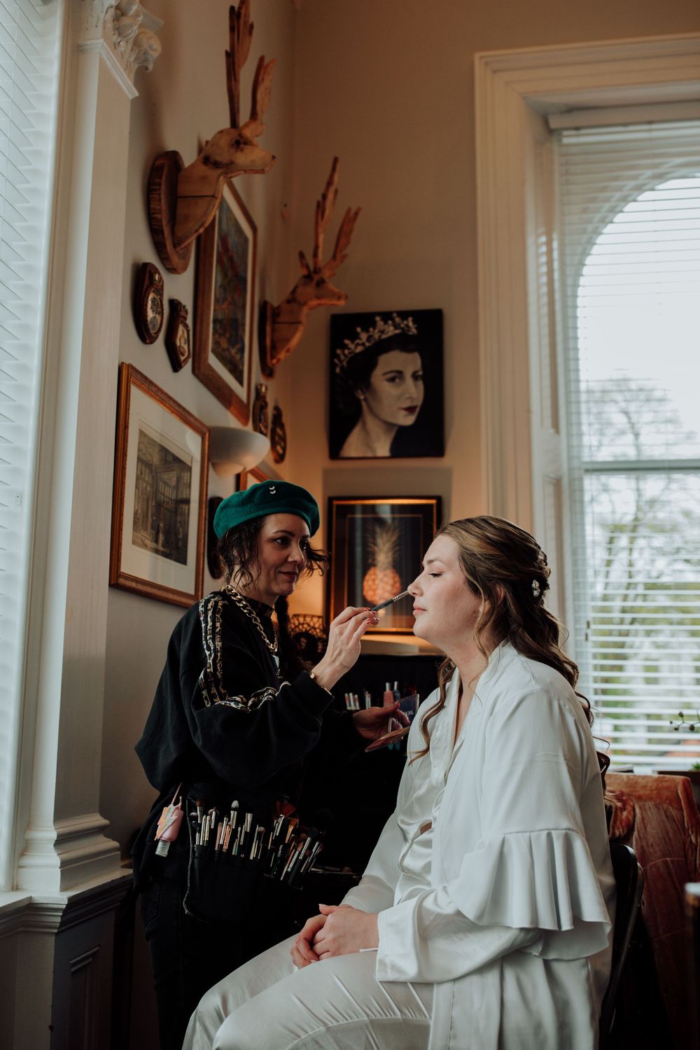 Makeup artist applies cosmetics to person in white robe during wedding preparation.