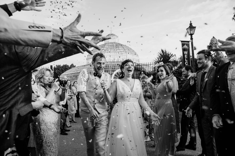 Celebratory confetti shower outside as newlyweds walk through crowds of guests.