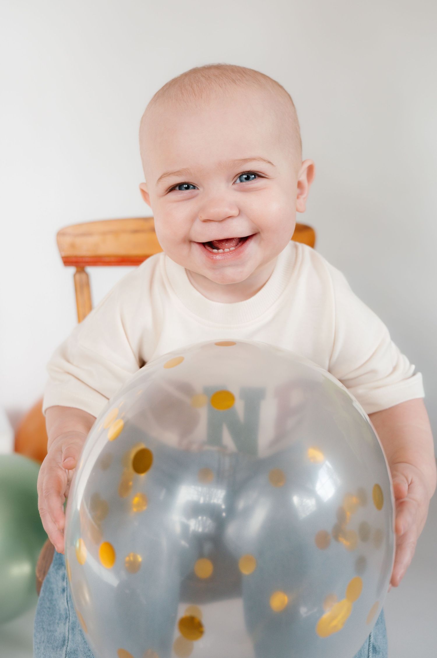 Smiling baby holding a clear balloon with gold confetti dots at their first birthday celebration.