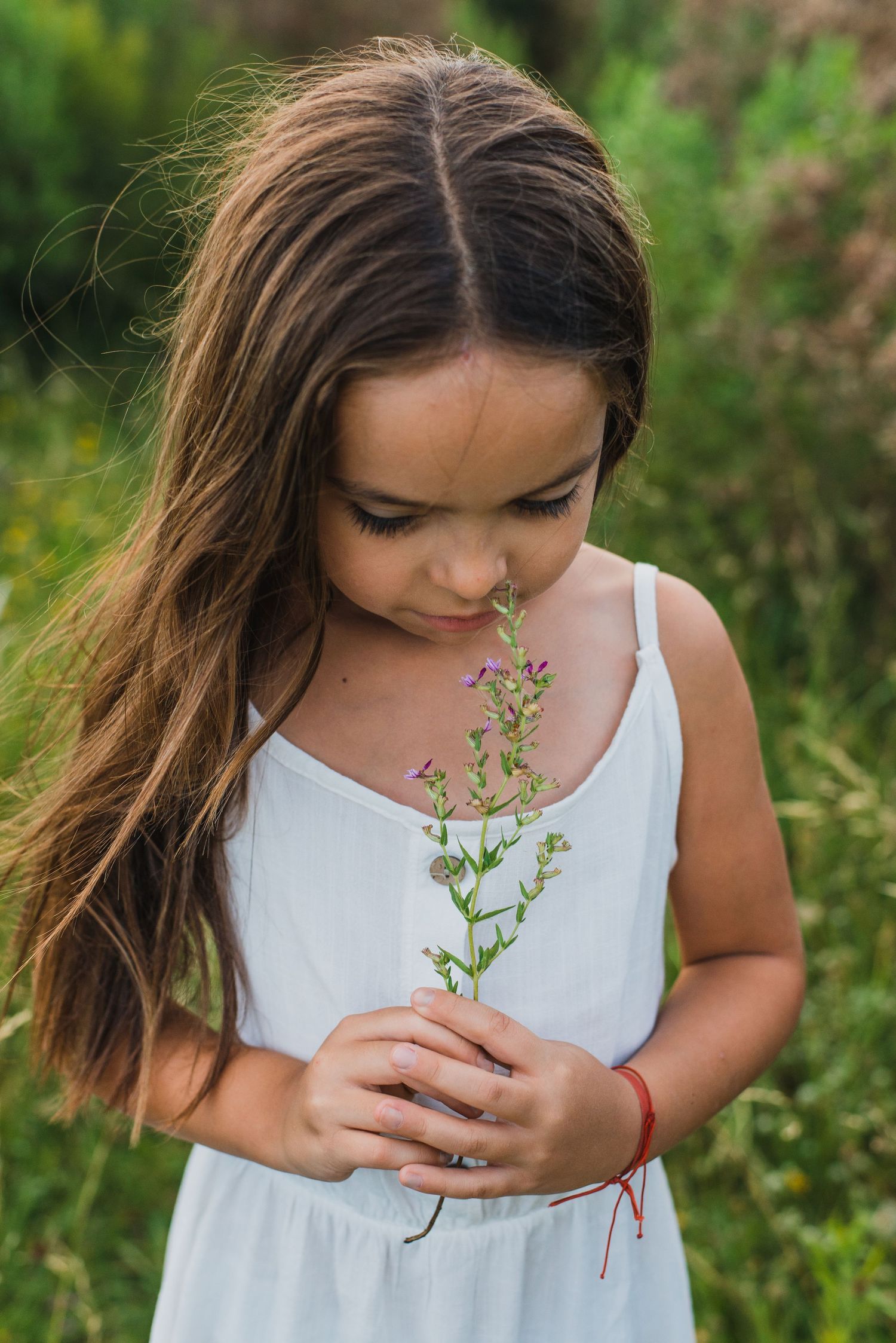 niña con vestido blanco oliendo una flor en un sesión familiar en exteriores durante el atardecer en Tandil