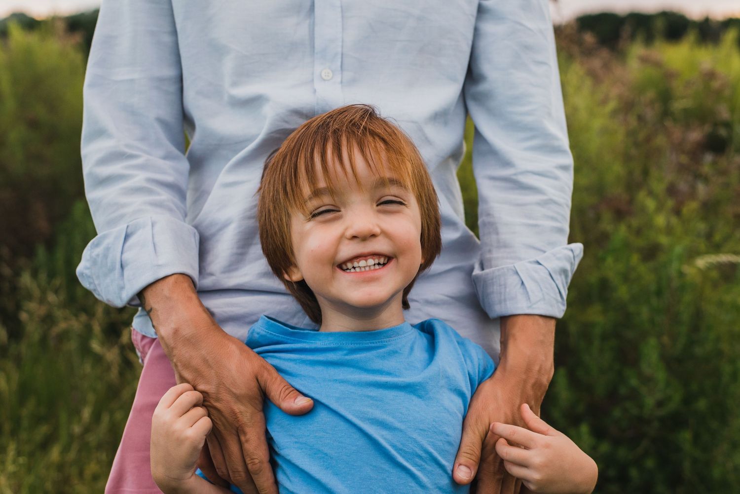Niño sonriendo en los brazos de su padre en un sesión familiar en exteriores durante el atardecer en Tandil