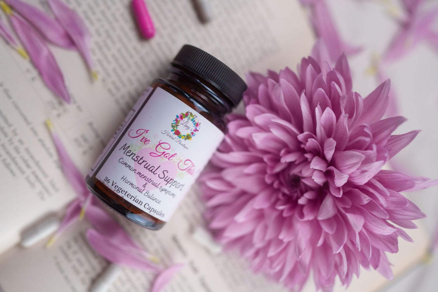 Natural supplement bottle with purple chrysanthemum flower on book pages.
