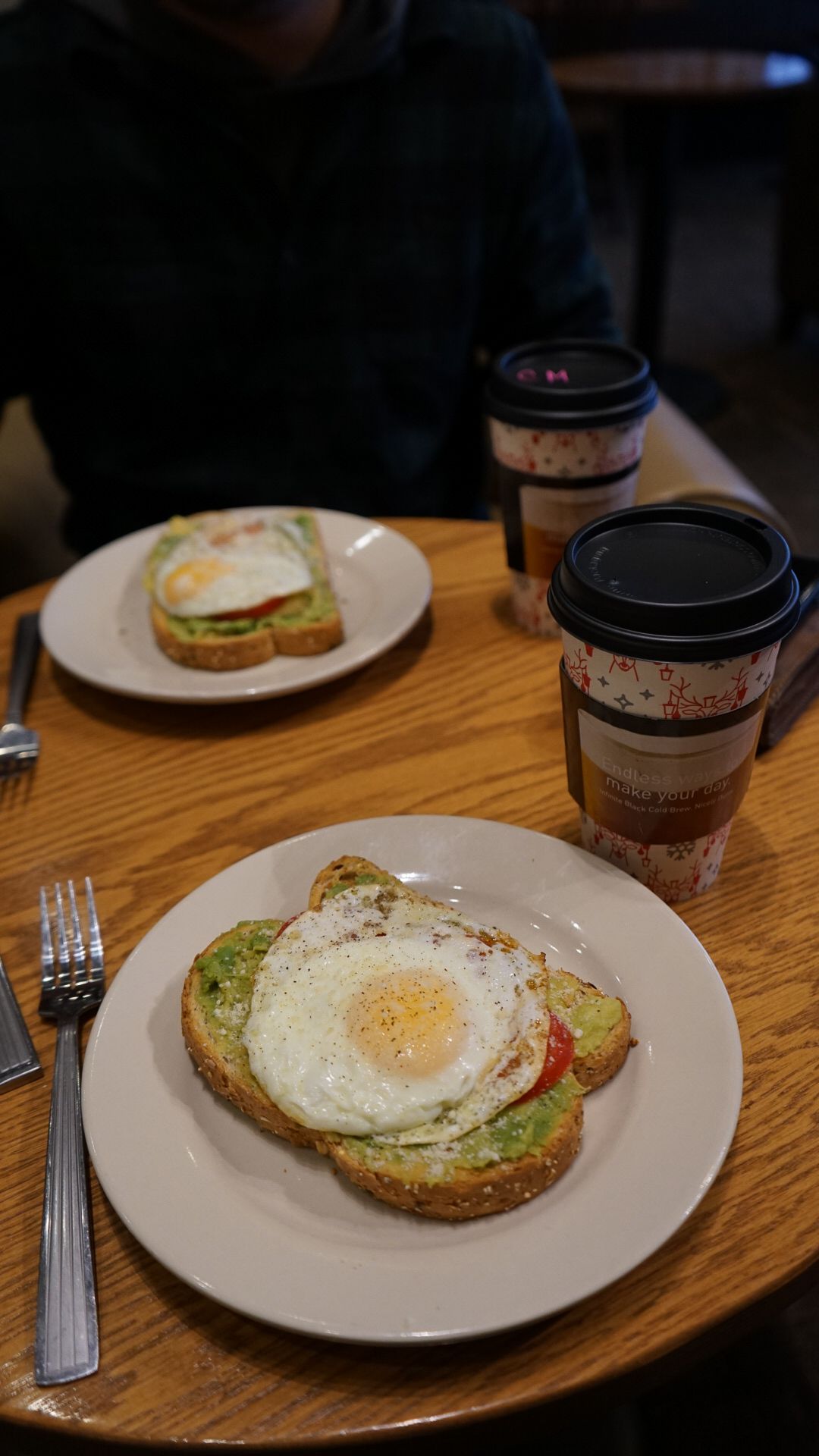 Breakfast plates with fried eggs and avocado toast served on wooden table.
