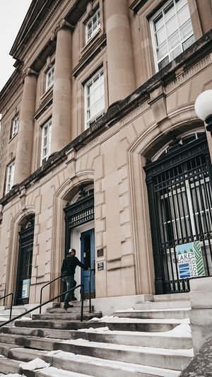 Stone building entrance with ornate steps and black iron railings in a classical architectural style.