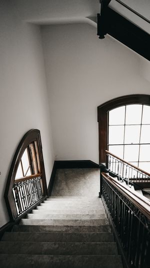 Interior stairwell with dark wooden banister and arched windows casting dramatic shadows.