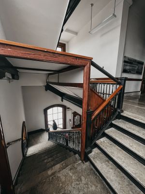 Interior stairwell with wooden railings and white walls in an old building.
