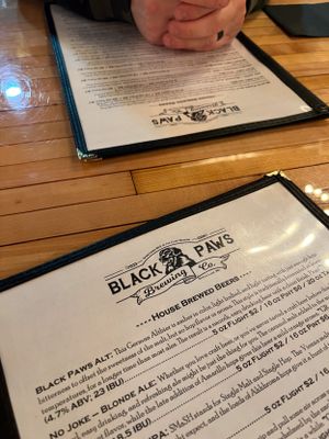 Black Paws Brewing Company menu displayed on wooden table showing beer and drink selections.