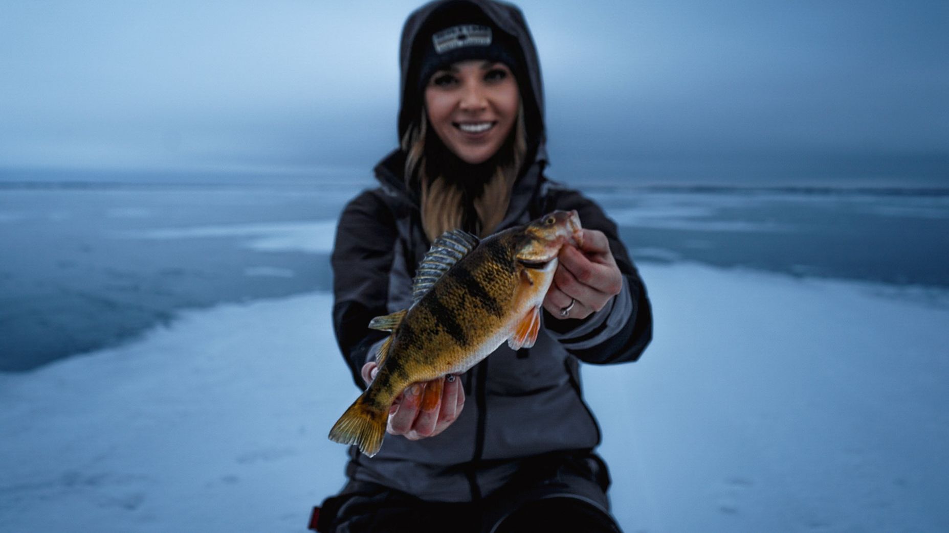 Ice fishing scene showing someone holding a yellow perch against snowy winter backdrop.