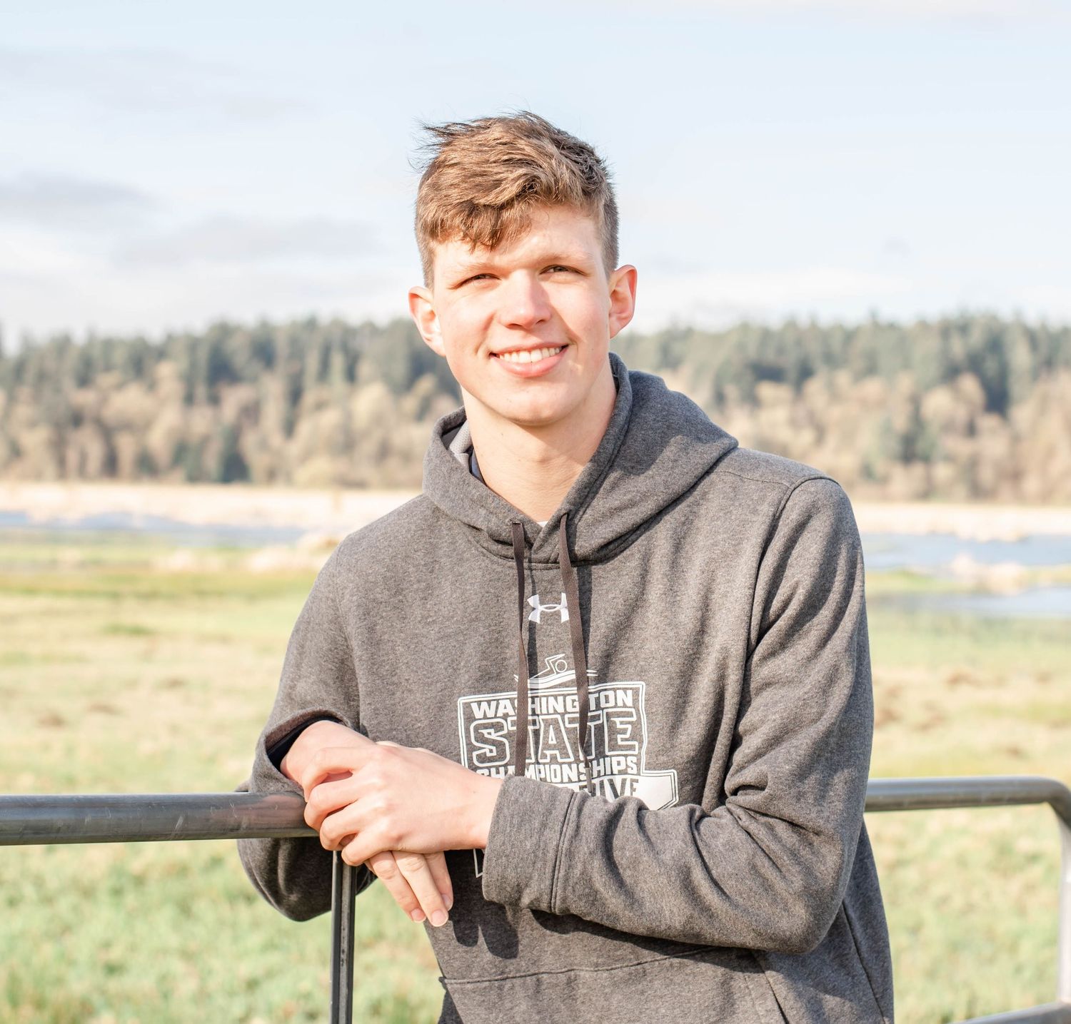 Person in grey hoodie leaning on railing with scenic waterfront view.