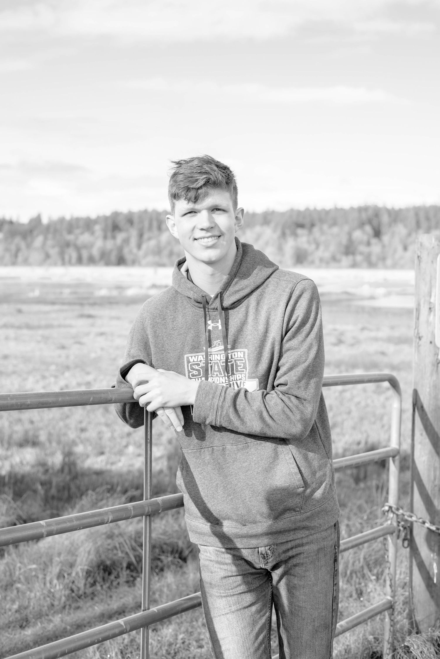 Person in grey sweatshirt leaning on a wooden railing in an outdoor rural setting.