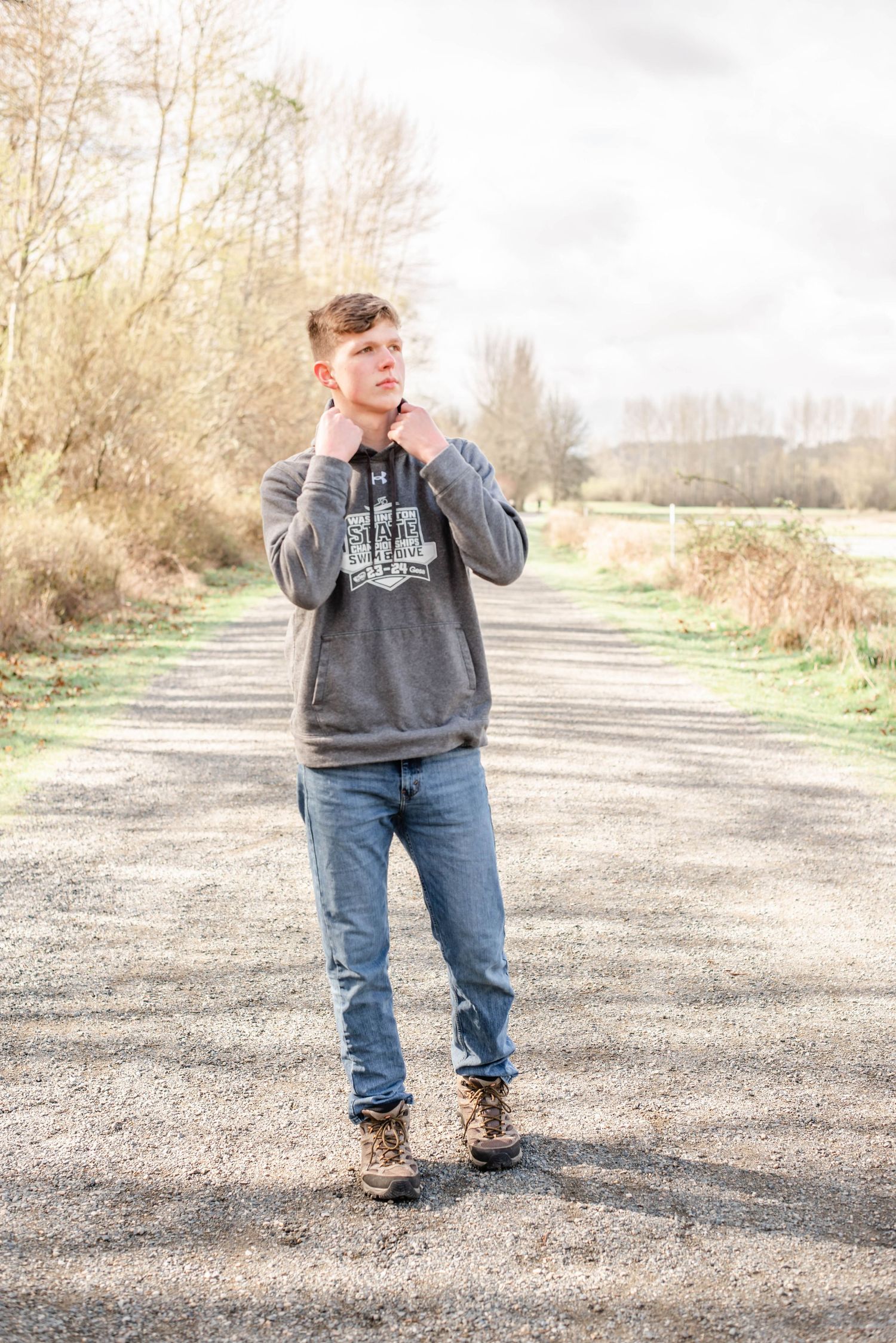 Person standing on gravel path wearing jeans and grey sweatshirt in rural setting.