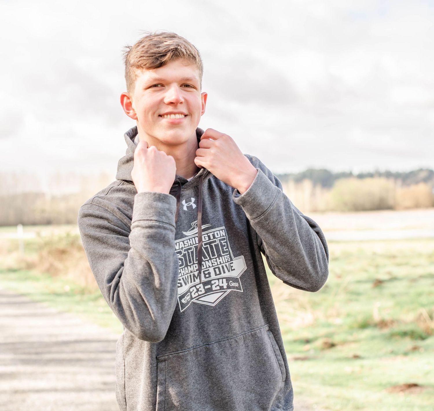 Person adjusting collar of grey hoodie sweatshirt outdoors.