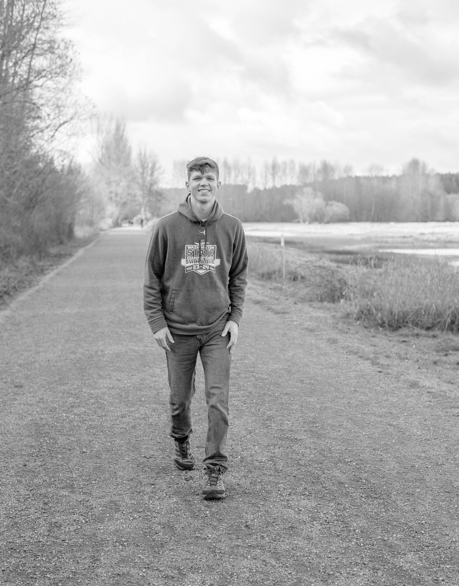 Person walking along grassy path surrounded by trees in black and white photo.