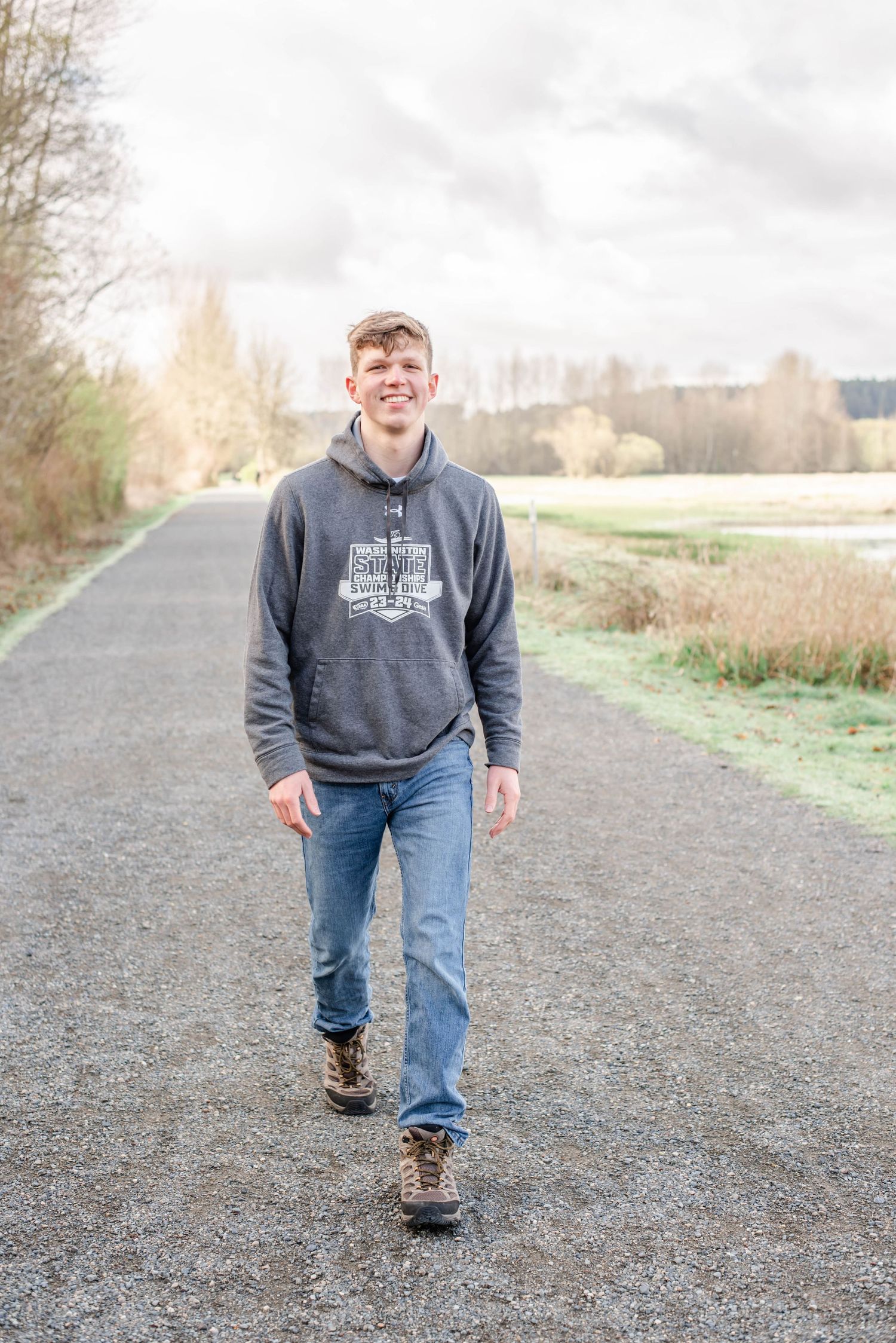 Person in grey hoodie walking on gravel path in natural setting.