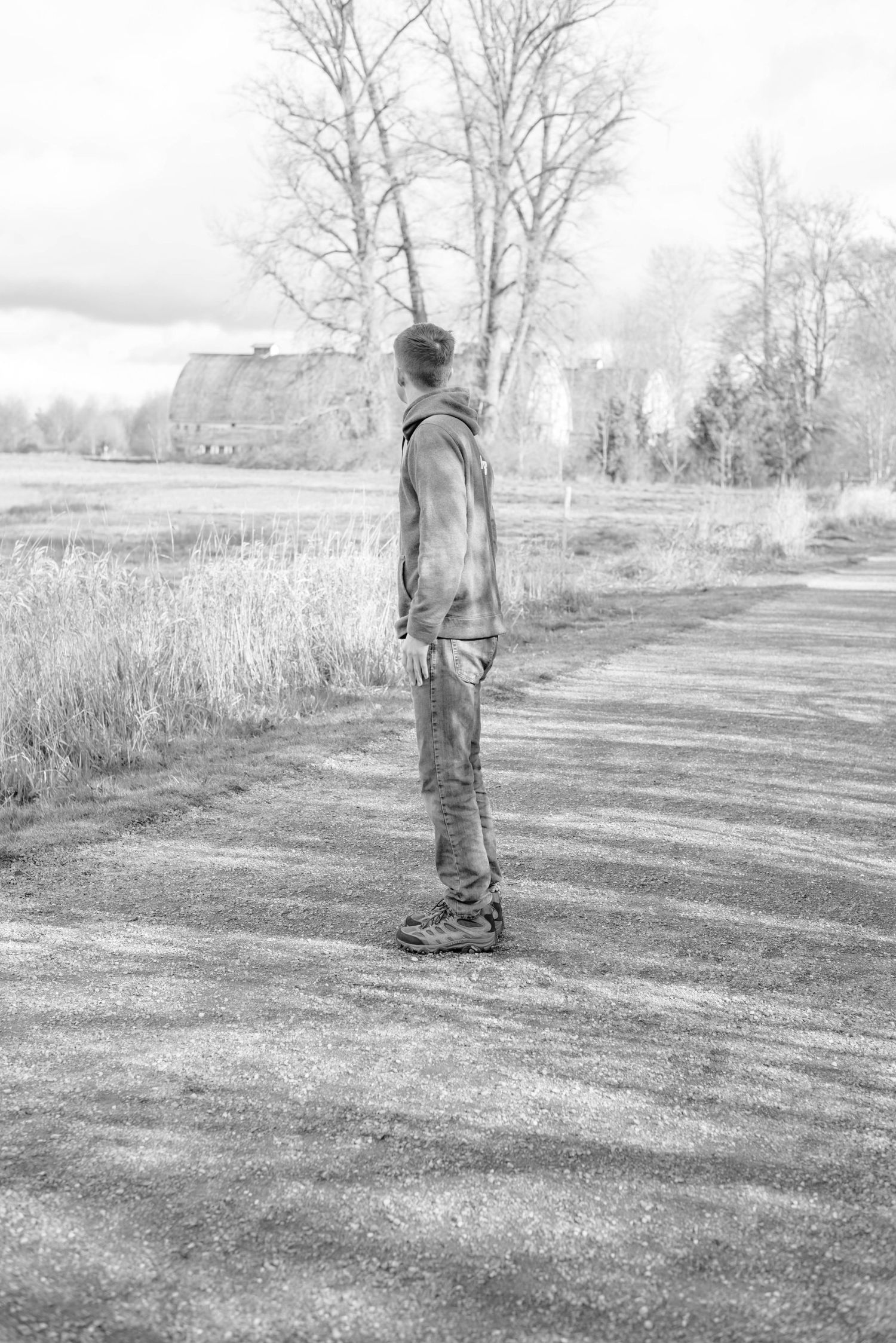 Person standing alone on rural path in black and white landscape photo.