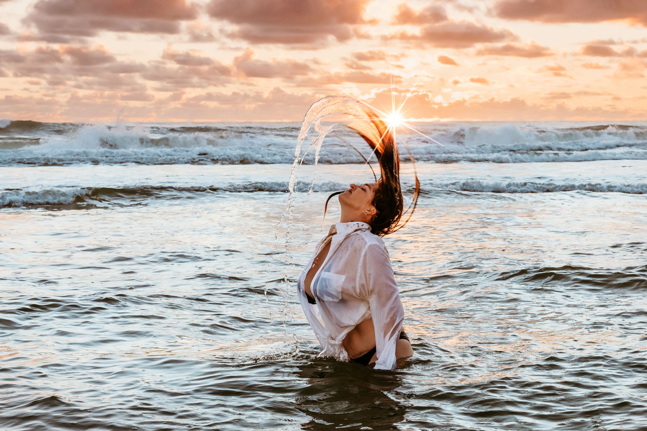 Person splashing in ocean waves during dramatic sunset.