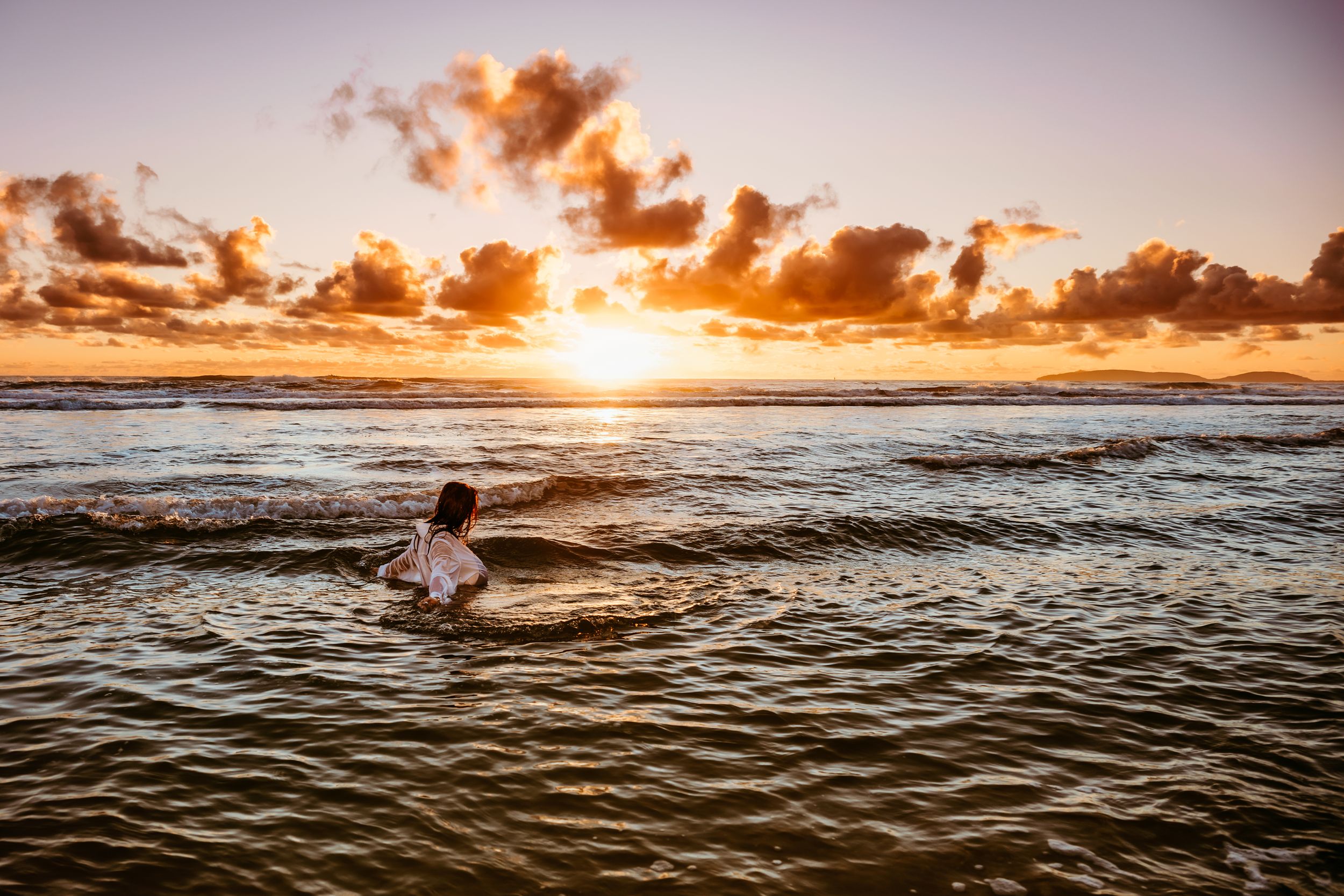 Silhouette of person swimming in ocean waves during golden sunset.
