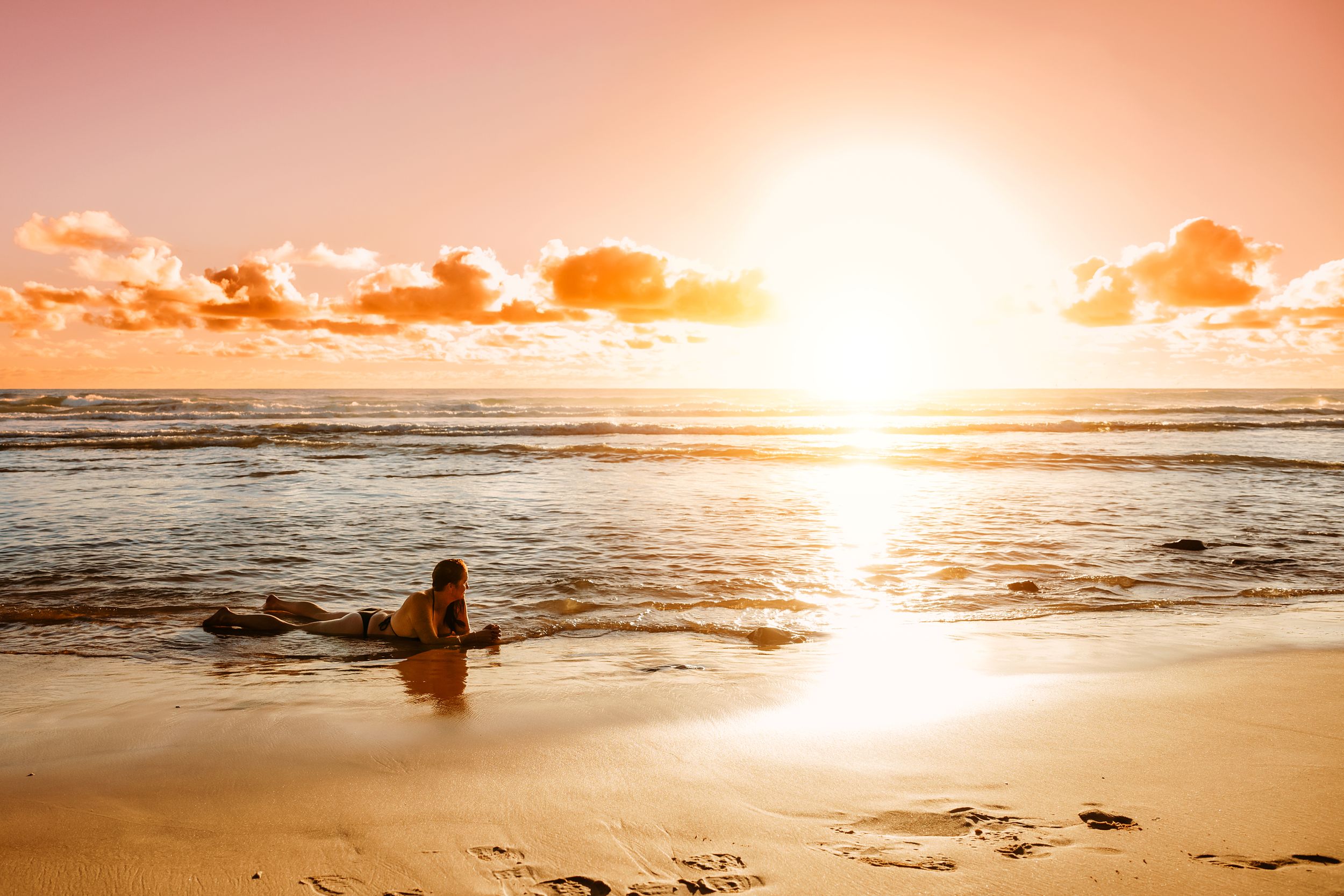 Silhouette of person on beach during golden hour with sun on horizon.