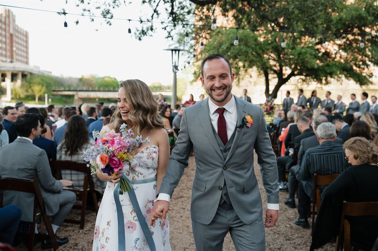 Newlyweds walking down the aisle together at an outdoor ceremony with colorful bouquet.