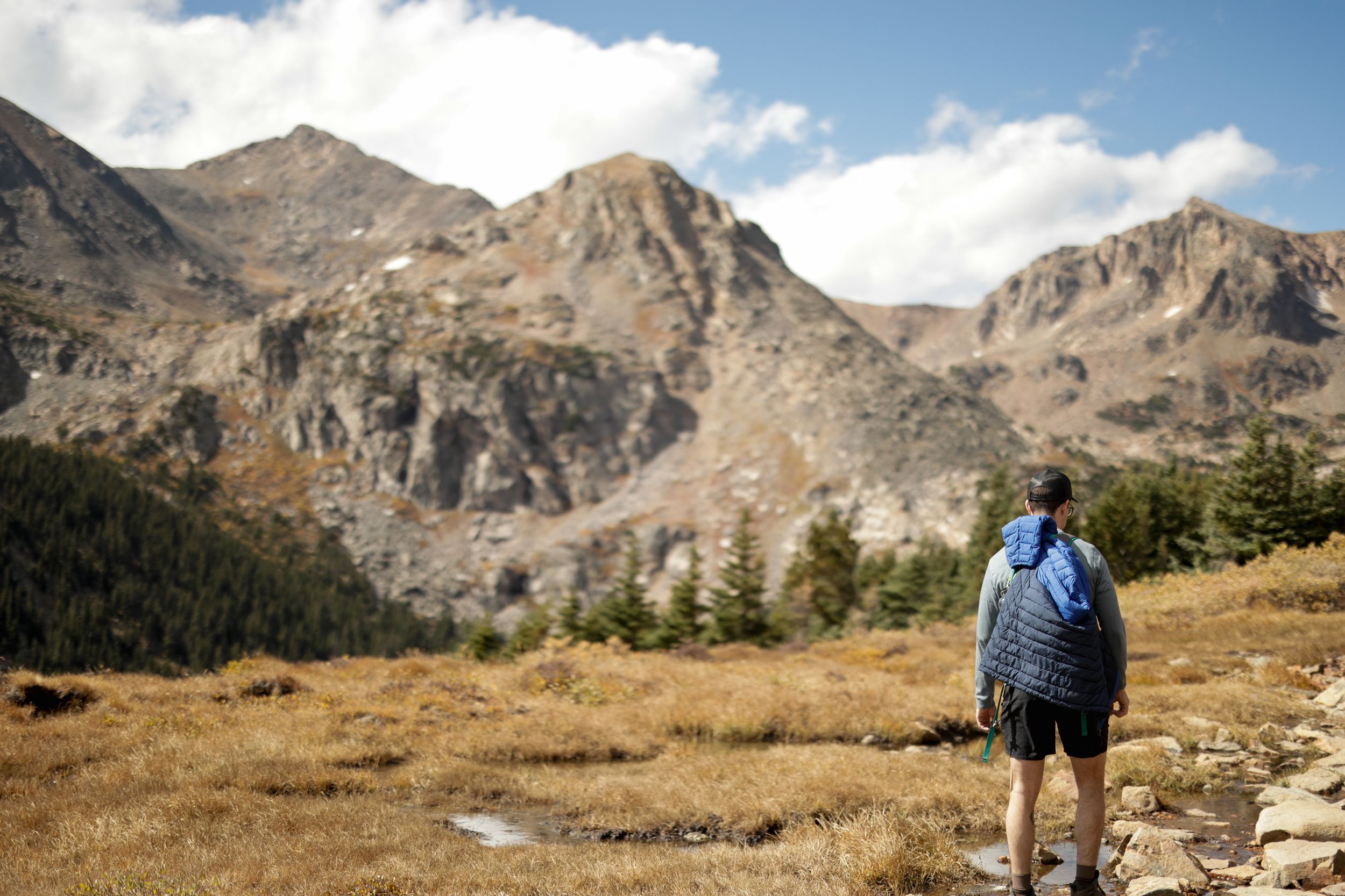 Hiker in blue jacket overlooks majestic rocky peaks and mountain landscape in a scenic wilderness area.
