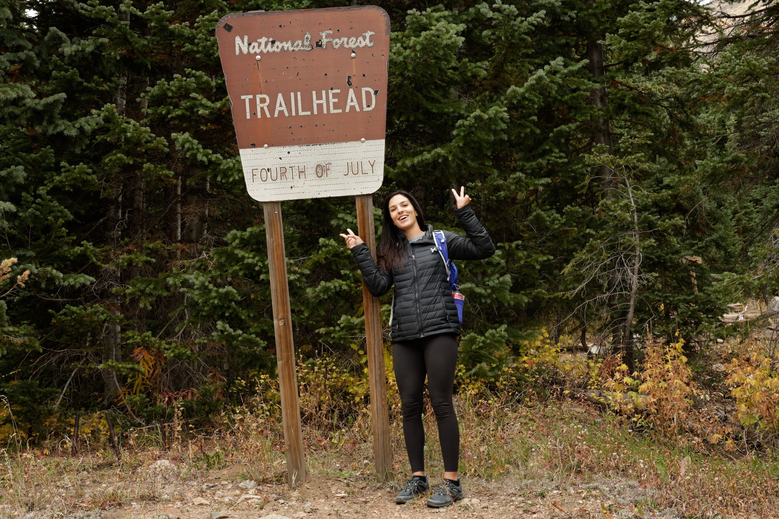 A person stands on a trail near rustic wooden trail marker signs in a wooded forest setting.