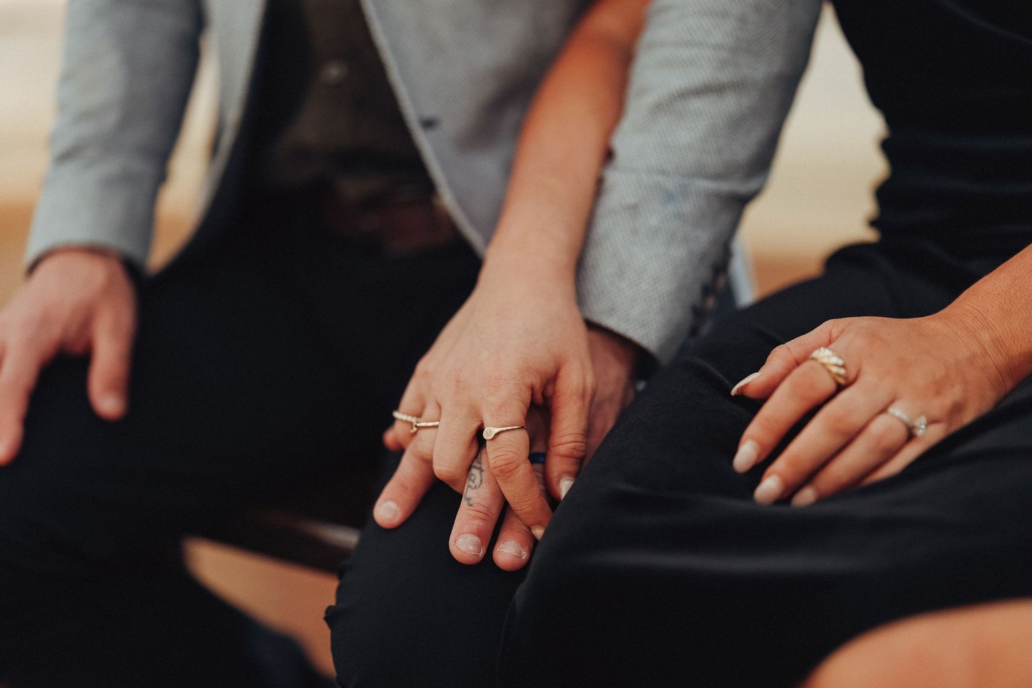 Close-up shot of hands wearing multiple delicate rings resting on dark fabric.