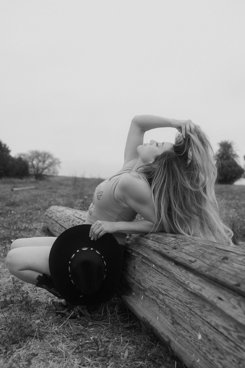 A person in black clothing reclines dramatically on a wooden log in a black and white photograph.