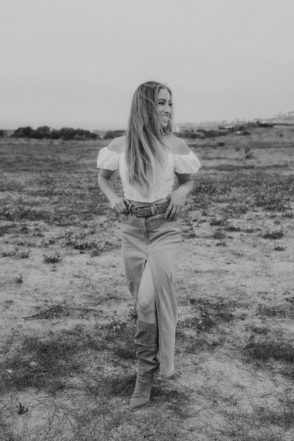 Black and white western-style portrait showing someone in boots and denim against an open field.
