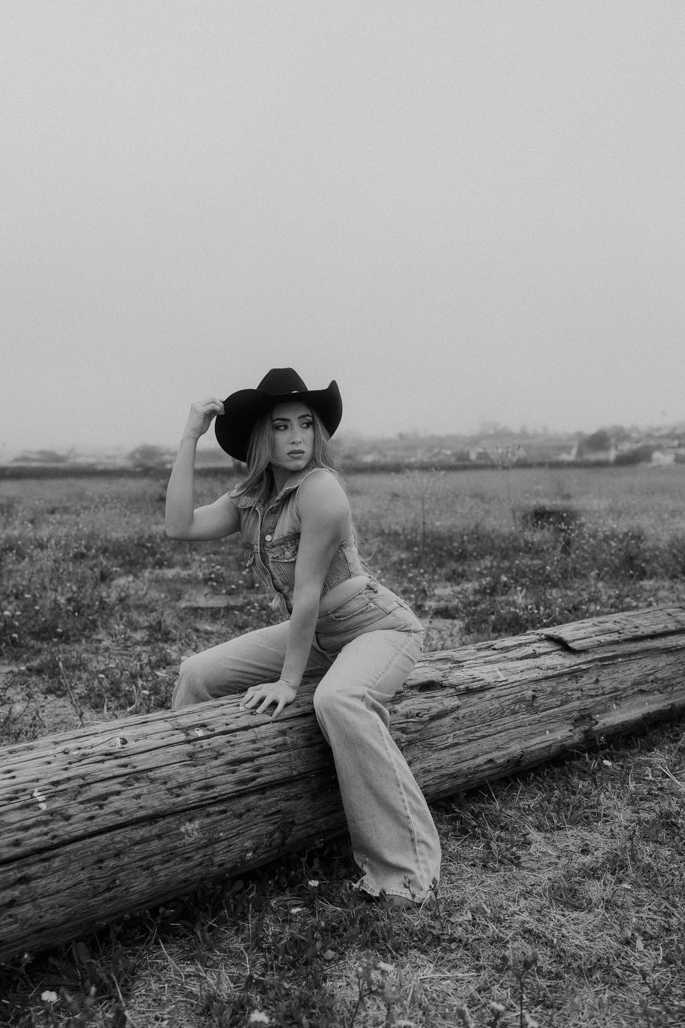 Vintage-style black and white portrait with western wear on a wooden log.