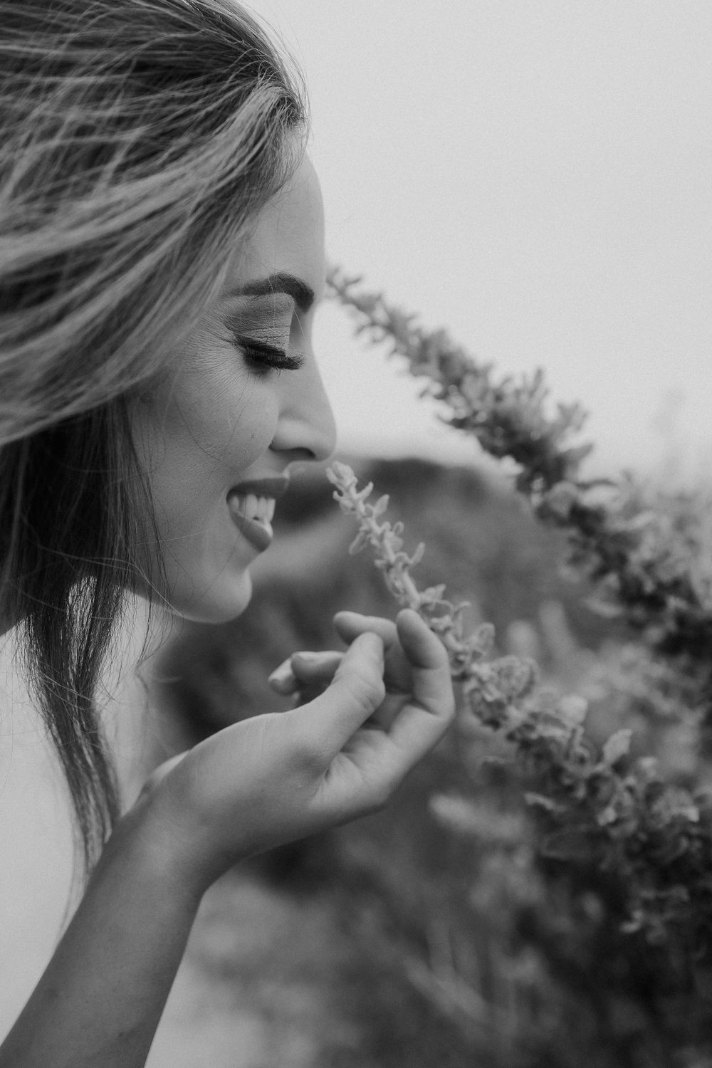 Artistic black and white close-up portrait showing a joyful expression near flowering plants.