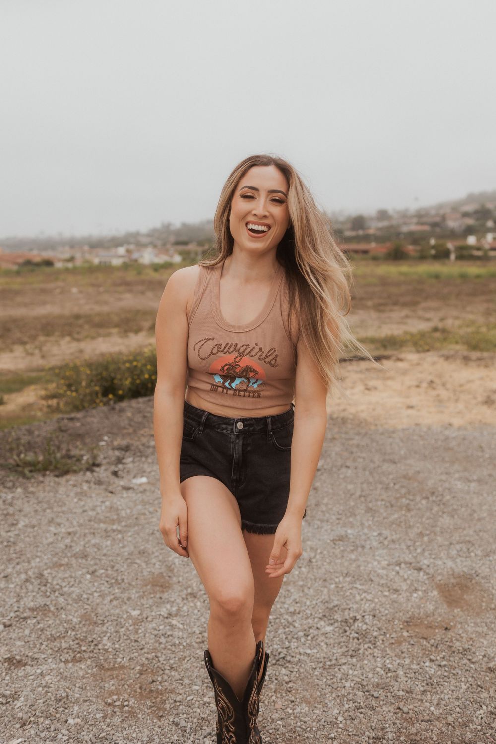A person in a casual tank top and denim shorts poses joyfully on a desert trail.