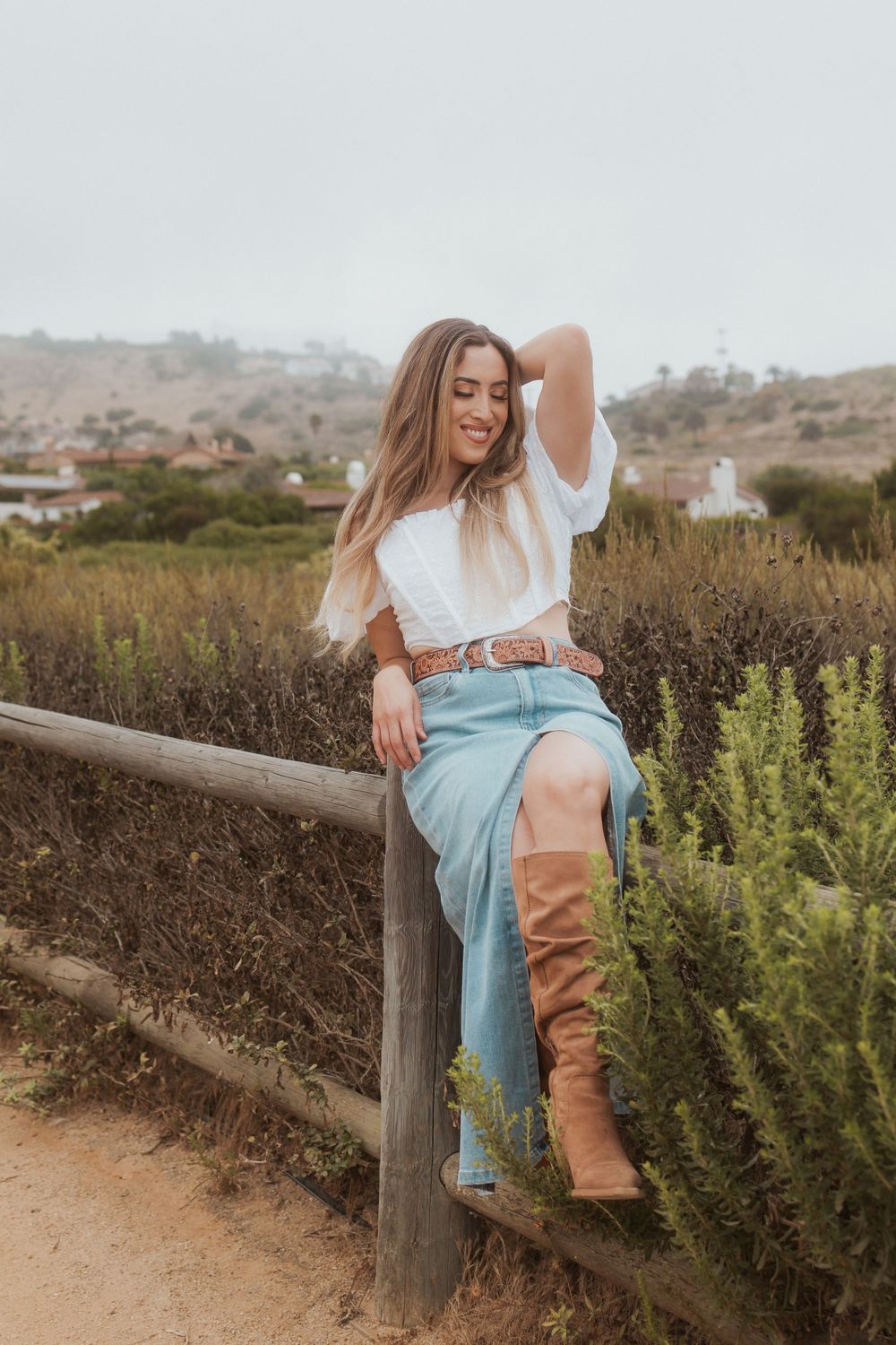 Rustic fashion portrait on a wooden fence with tan boots and a denim skirt.