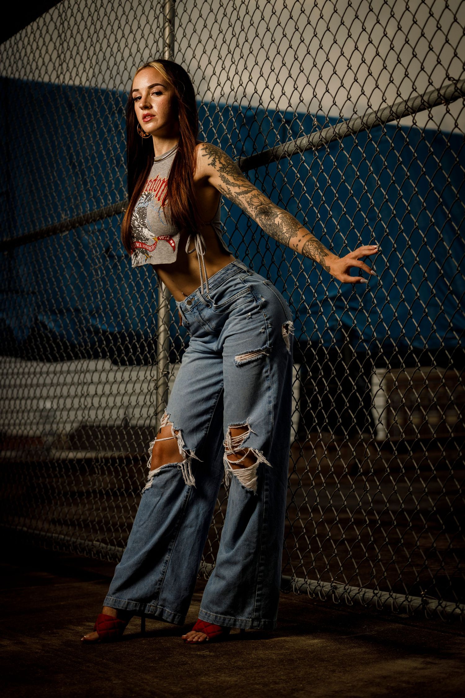 Urban fashion portrait against chain link fence with dramatic lighting.