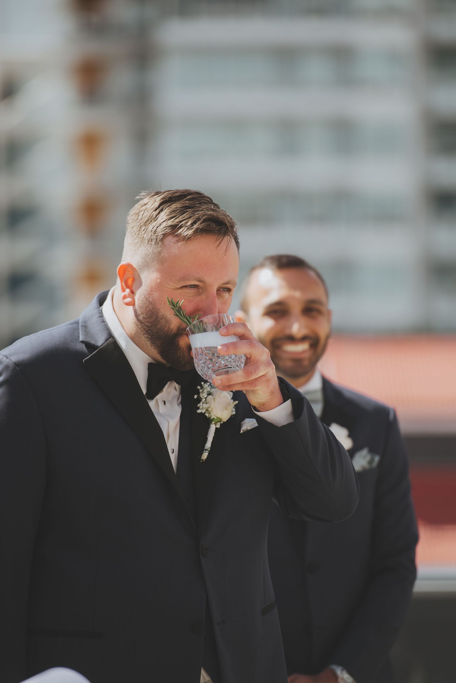 Two groomsmen in black tuxedos share a lighthearted moment during wedding celebrations.
